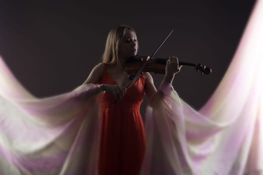 Studio shot of beautiful woman playing violin, on gray background
