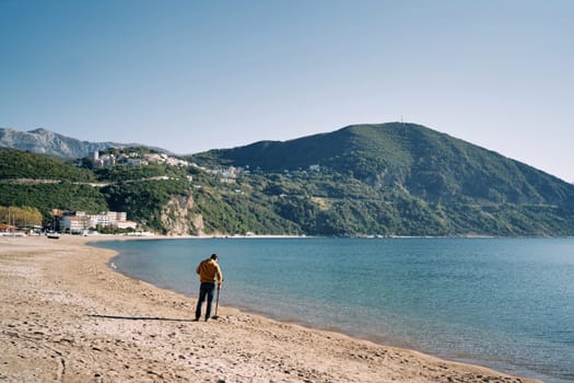 Man swipes a metal detector over the sand while walking along the beach near the sea. High quality photo