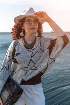 Stylish seashore woman. Fashionable woman in a white hat, white trousers and a light sweater with a black pattern on the background of the sea