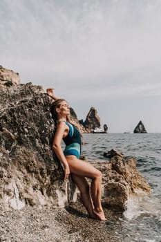 Woman beach vacation photo. A happy tourist in a blue bikini enjoying the scenic view of the sea and volcanic mountains while taking pictures to capture the memories of her travel adventure