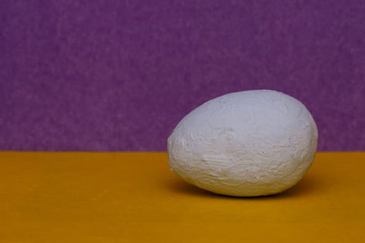 A light blue hand painted decorative egg on a yellow and purple background.copy space