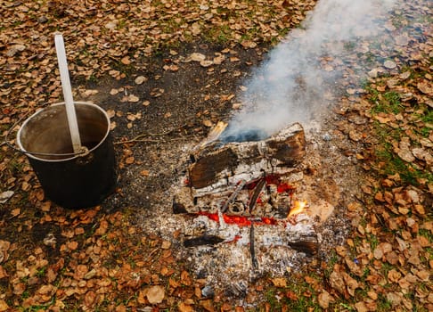 Black cauldron with cooked food near the fire against the background of autumn fallen leaves.