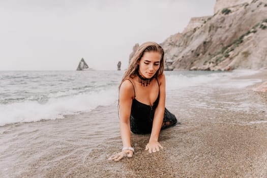 Woman travel sea. Young Happy woman in a long red dress posing on a beach near the sea on background of volcanic rocks, like in Iceland, sharing travel adventure journey