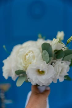 A bouquet of white flowers is being held by a person. The flowers are arranged in a vase and are placed on a blue background. The bouquet has a simple and elegant design