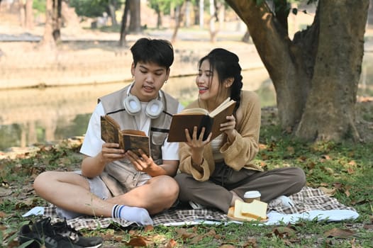 Young couple having picnic on the lawn in summer park and reading book.