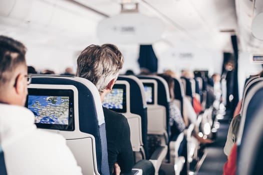 Interior of airplane with passengers on seats and stewardess in uniform walking the aisle, serving people. Commercial economy flight service concept