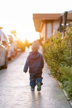 Little girl walks along a sunny sidewalk along parked cars. Back view. High quality photo