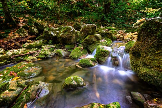 Close up view of water stream between rocks with green moss.