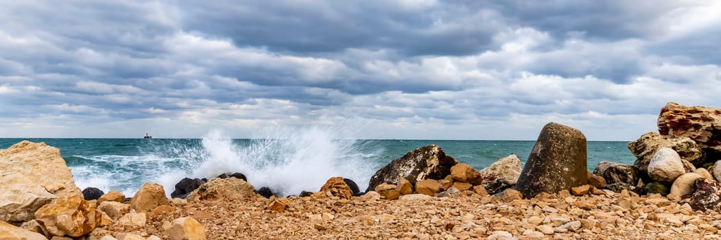 Wave splash at rocky shore and scenic clouds. Banner view