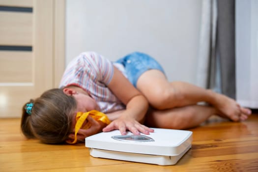 Distressed young girl lying on the floor next to a weighing scale and measuring tape. Body image and weight loss concept. Design for health and wellness poster, banner, flyer.