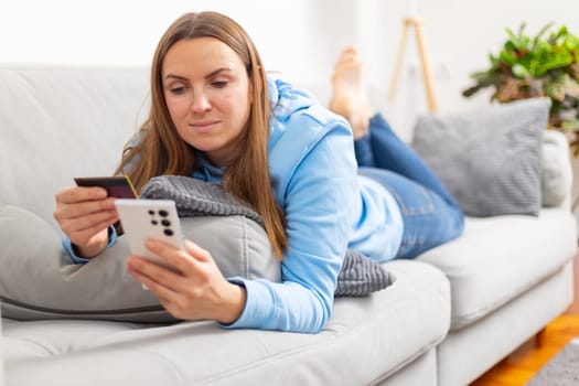 Woman in blue hoodie using credit card and smartphone. Casual indoor portrait with natural light and copy space for design and print.