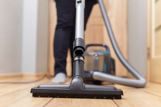 Person vacuuming wooden floor. Household chore and cleaning concept. Design for banner, poster, brochure, advertisement.