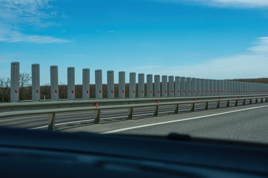 A road with a long line of metal posts with red hearts on them. The road is empty and the sky is clear