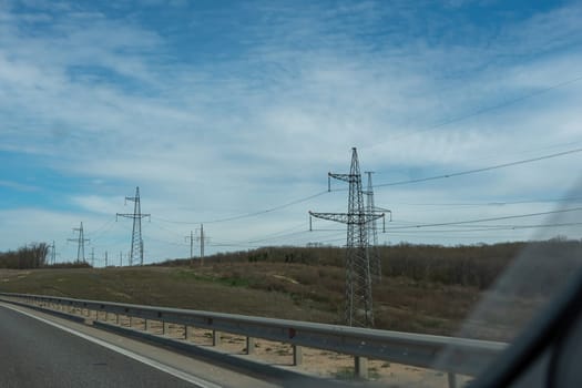 A road with a power line running along it. The sky is blue and there are some clouds.