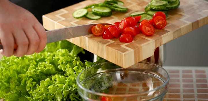 Cook holds knife in hand and cuts on cutting board red tomatoes for salad or fresh vegetable soup with vitamins. Raw food and vegetarian recipe book in modern society popular concept.