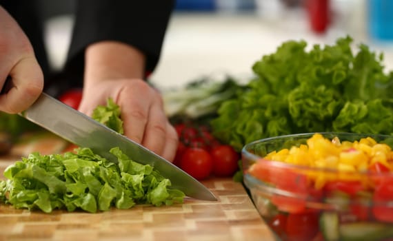 Cook holds knife in hand and cuts on cutting board green for salad or fresh vegetable soup with vitamins. Raw food and vegetarian recipe book in modern society popular concept.