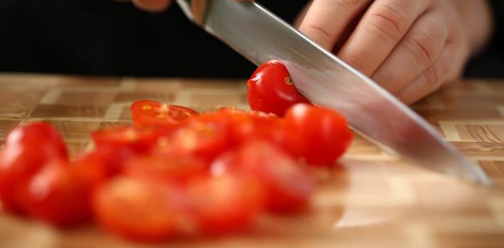 Cook holds knife in hand and cuts on cutting board red tomatoes for salad or fresh vegetable soup with vitamins. Raw food and vegetarian recipe book in modern society popular concept.