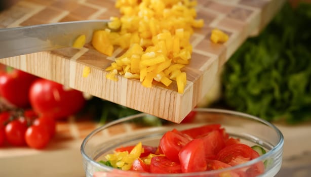 Cook holds knife in hand and cuts on cutting board yellow pepper for salad or fresh vegetable soup with vitamins. Raw food and vegetarian recipe book in modern society popular concept.