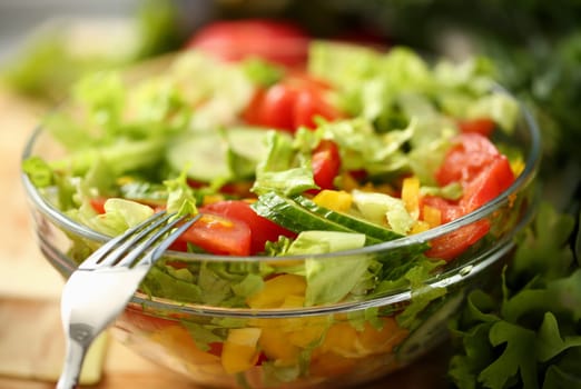 Silver fork in plate mixes salad fresh vegetables seasoned with olive oil. Raw food and vegetarian in modern society is popular concept.