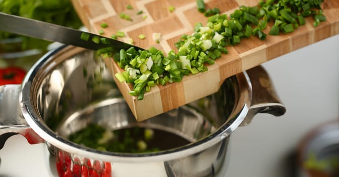 Cook holds knife in hand and cuts on cutting board green onions for salad or fresh vegetable soup with vitamins. Raw food and vegetarian recipe book in modern society popular concept.