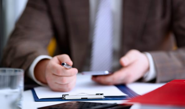 Male arm in suit hold phone and silver pen at workplace closeup. Read news mania send sms chat addict use electronic bank modern lifestyle job plan colleague share blog tweet web application search