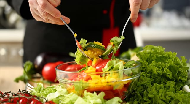 Cook holds fork in hand and mixes salad fresh vegetables seasoned with olive oil. Raw food and vegetarian in modern society is popular concept.