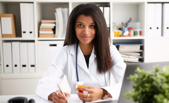 Female black medicine doctor hand hold jar of pills and write prescription to patient at worktable. Panacea and life save, prescribing treatment legal drug store concept. Empty form ready to be used