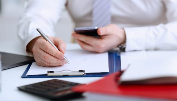 Male arm in suit and tie hold silver pen filling schedule in notepad at office workplace closeup. Legal law consult assistance gesture or finance investment advisor clerk job information gesture