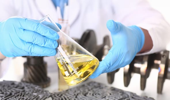 Male hands in protective gloves hold test tube in hands produces chemistry test of motor oil automatic gearbox and hydraulic booster