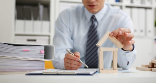 Male hand holds the roof to the lock in the hand against the backdrop of the toy house sale purchase lease concept real estate services on the market.