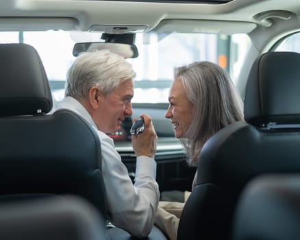 Mature Caucasian couple sitting in a new car and rejoicing at the purchase