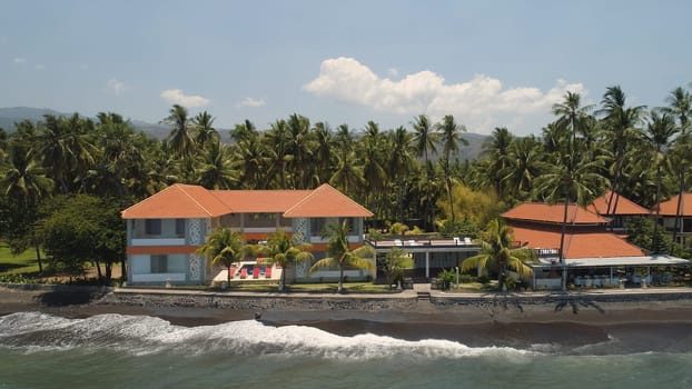 aerial view luxury hotel with swimming pool, sun beds, palm trees by sea. seascape coastline with black sand beach, palm trees, hotel, tropical resort. Bali,Indonesia, travel concept.