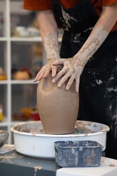Close-up of a potter's hands making a ceramic vase on a potter's wheel. Vertical photo