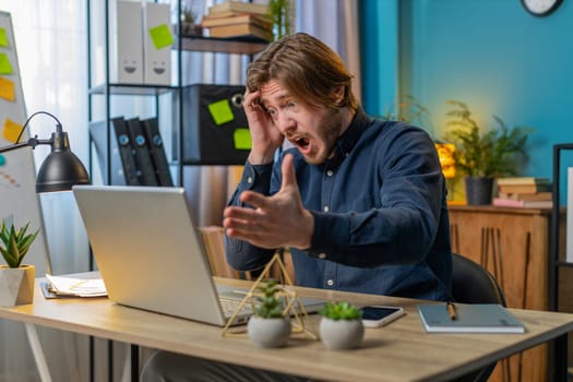 Displeased sad businessman using laptop notebook typing browsing working loses becoming surprised sudden lottery results bad news fortune loss game fail computer virus. Caucasian guy at home office.