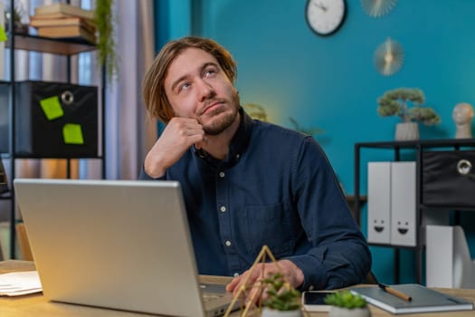 Thoughtful concerned businessman working on laptop computer looking away thinking solving problem at home office table. Serious freelancer search for inspiration make decision feel lack of ideas.