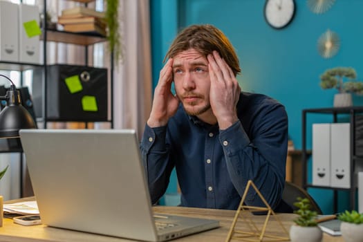 Tired ill Caucasian businessman suffering from headache problem tension and migraine, stress at home office table workplace. Bearded freelancer broker worker man works on laptop notebook. Overworking