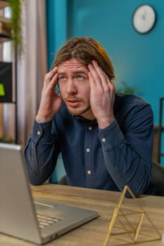 Tired ill businessman suffering from headache problem tension and migraine, stress at home office desk workplace. Bearded freelancer broker worker man works on laptop notebook. Overworking. Vertical