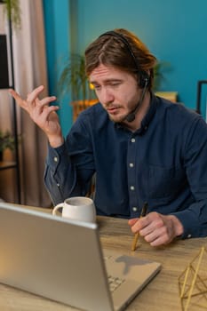 Businessman wearing headset, freelance worker, call center or support service operator helpline, talking with client or colleague communication support. Happy man sits at home office desk. Vertical