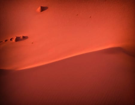 The image is a sand dune with footprints in the foreground.