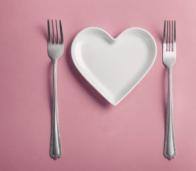 The image shows a heart-shaped plate with two forks and a knife on top of it.