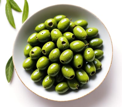 The image shows a bowl of green olives on a white plate, surrounded by leaves.