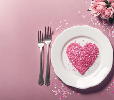 The image shows a plate with a heart shaped cake on it, surrounded by pink roses and two forks.