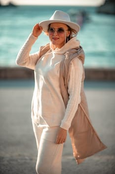 Happy blonde woman in a white suit and hat posing at the camera against the backdrop of the sea.