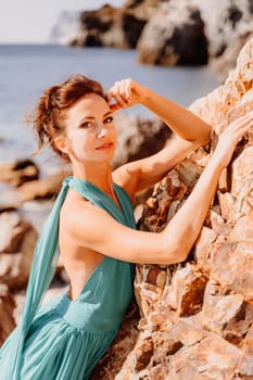 Woman green dress sea. Woman in a long mint dress posing on a beach with rocks on sunny day. Girl on the nature on blue sky background