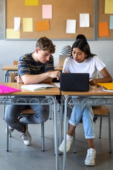 Caucasian teen boy and native american teenage female high school students in class working together on school project using laptop. Vertical image. Education concept.