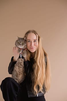 A woman natural blonde long hair smiling in a black clothes stand, sitting on photo studio. girl with pet scottish straight cat. portrait , vertical, close up