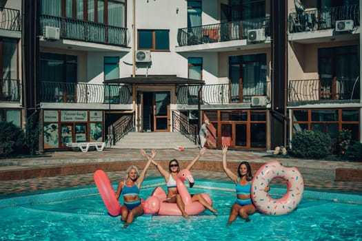 Three women are in a pool with inflatable toys, including a pink flamingo and a donut