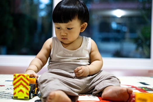 Close up of little boy in casual clothes sitting on floor and playing toy trucks while spending free time at home.