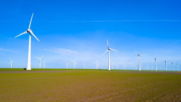 A vast expanse of land in Flevoland, Netherlands, is covered with a plethora of towering windmills spinning in unison under the vibrant Spring sky. windmill turbines green energy