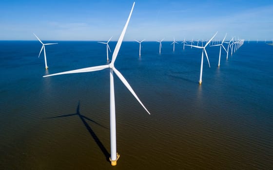 A group of elegant windmills hover gracefully above the calm, reflective surface of the water in Flevoland during the vibrant season of Spring. drone aerial view of windmill turbines green energy